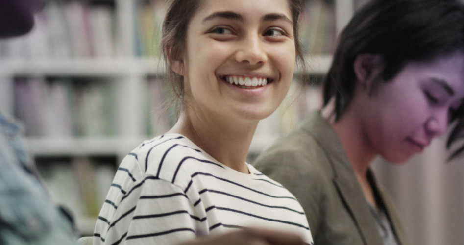 Une étudiante souriante travaille aux côtés de ses camarades en salle de cours.