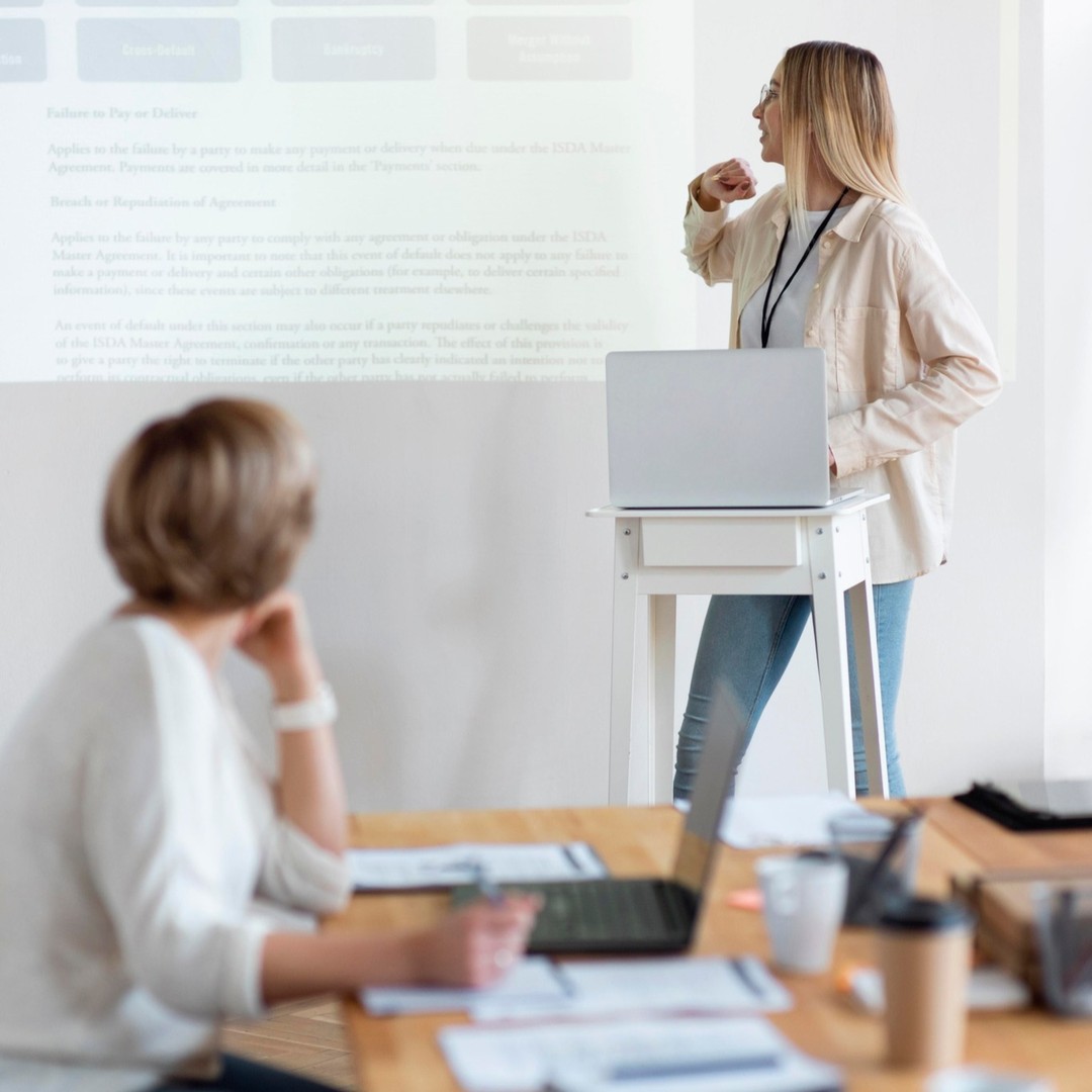 Une intervenante présente un cas en salle de cours, devant des participants équipés d’ordinateurs.