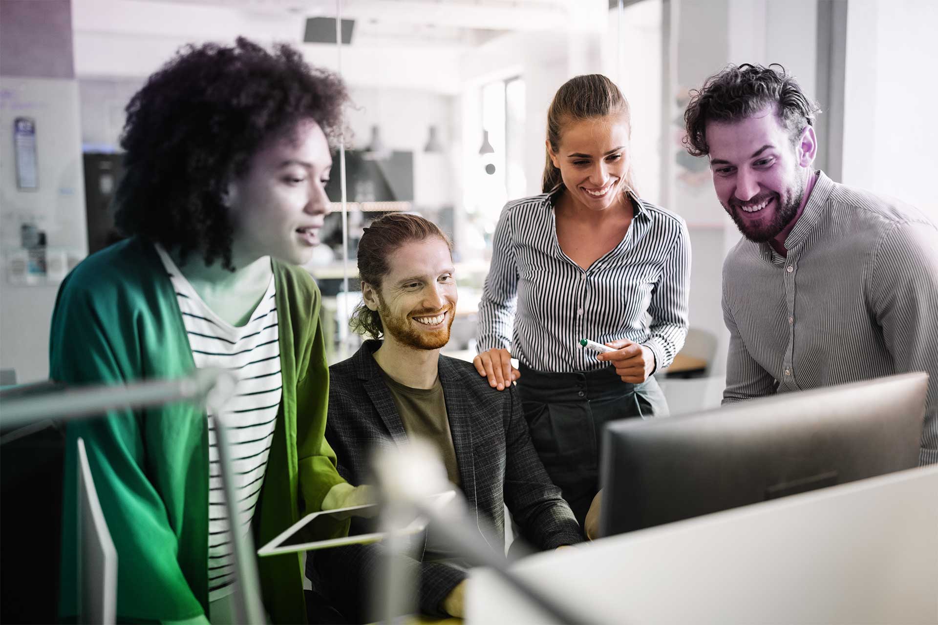 Quatre jeunes adultes collaborent autour d’un écran dans un espace de travail lumineux.