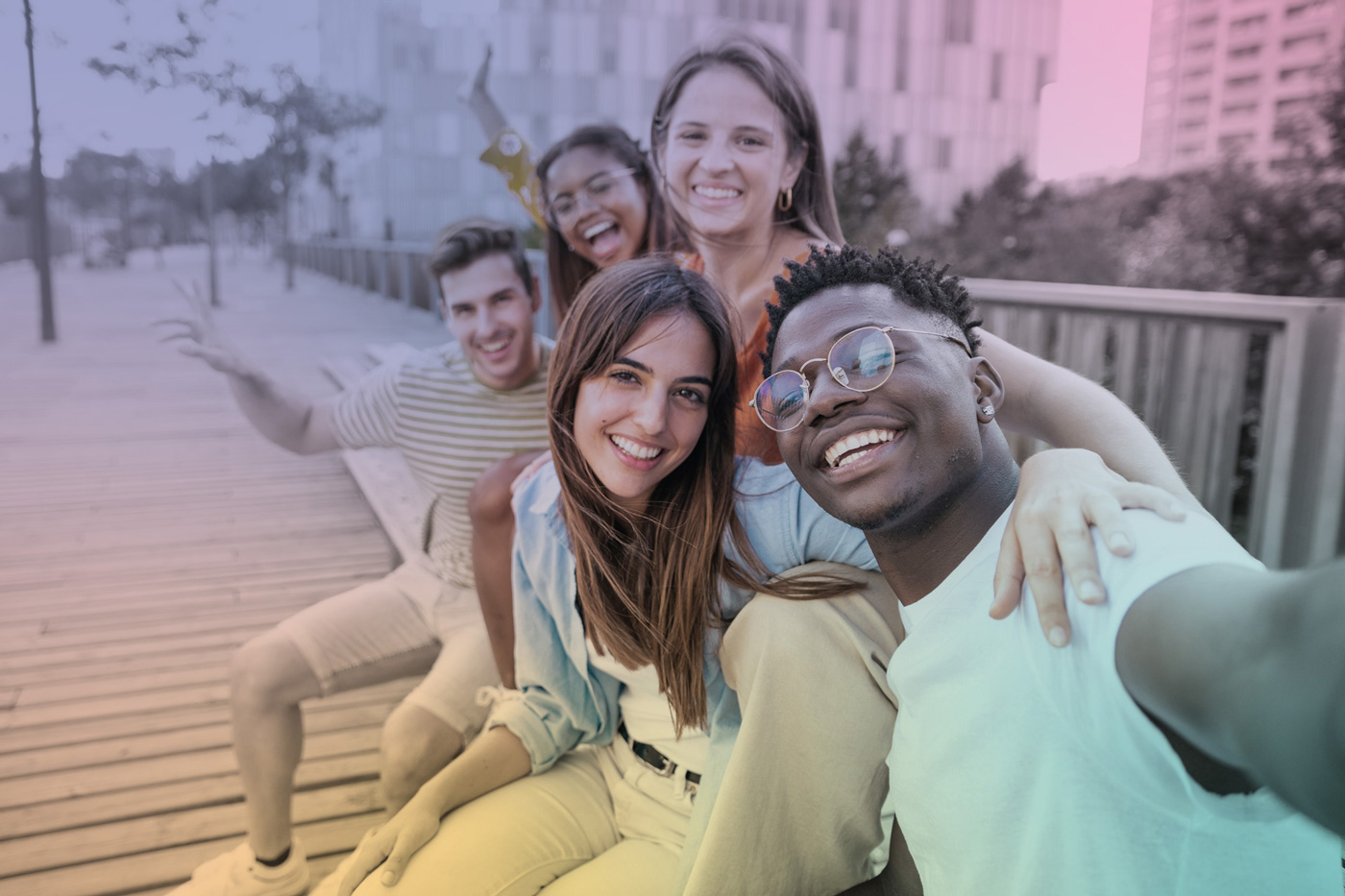 Cinq jeunes adultes souriants partagent un moment ensemble sur une passerelle urbaine.