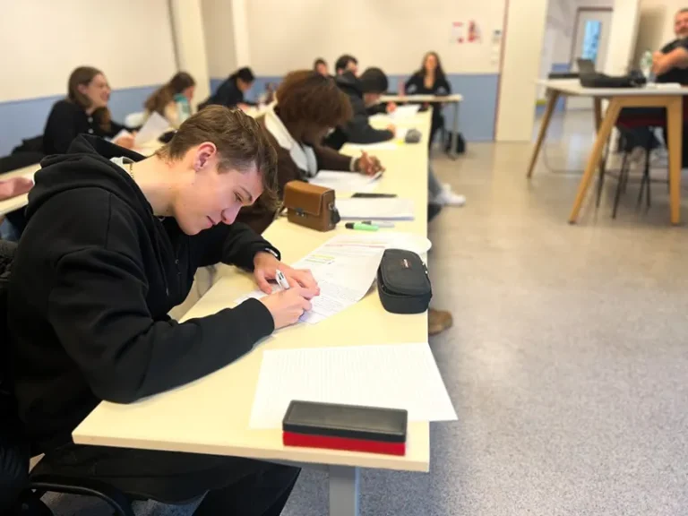 Un étudiant prend des notes, entouré de ses camarades en salle de cours.